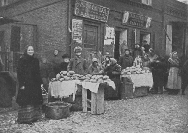 several men and women standing with bread-covered tables in front of brick building