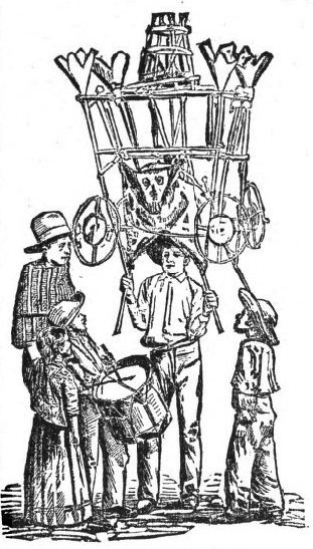 group of adults and children, one holding up some kind of sculpture made of sticks with what appears to be a mask on it. one child plays a drum
