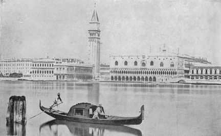 two men in a gondola with a view of the city across the water behind them.