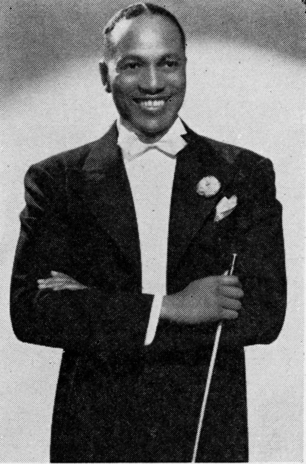photograph of Andy Kirk smiling in a suit with a flower in the lapel. he holds a baton in his hand