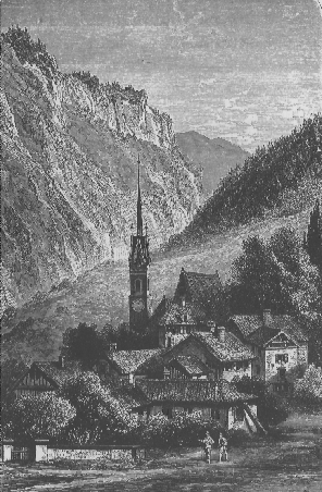 a cluster of buildings in a small valley. two people stand outside talking