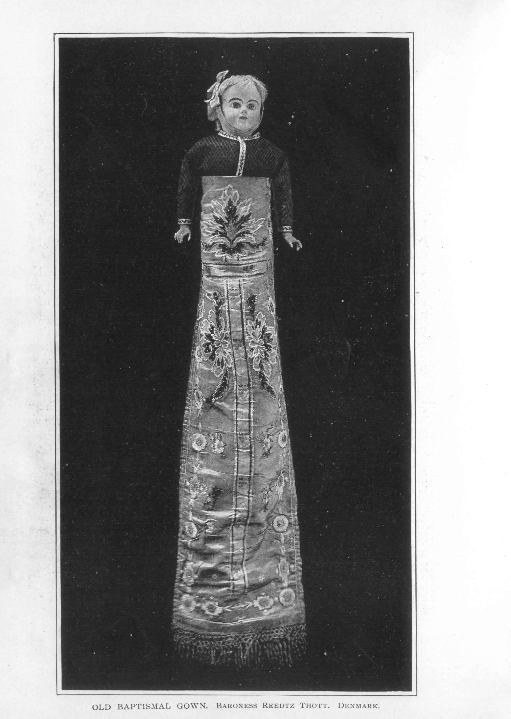 infant gown embroidered with floral design, displayed on a doll