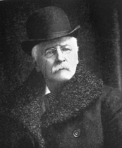 Photograph of man in coat and bowler hat with mustache and glasses
