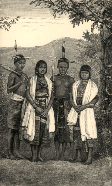 Four young people standing, two male, two female. They are all wearing skirts. The men have headdresses and spears, the women have longer hair, long white scarves and wear many necklaces. They are amidst some trees with mountains in the background.
