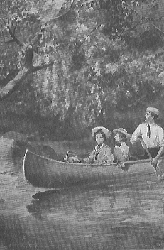 man paddling a canoe with two children in it down a tree-lined river