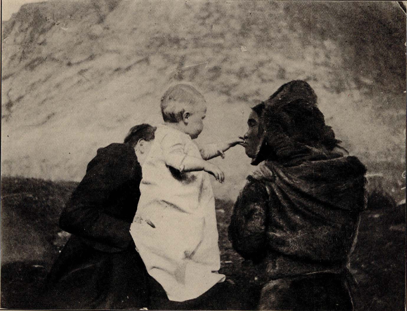Woman holding baby, whose hand is being kissed by another woman.