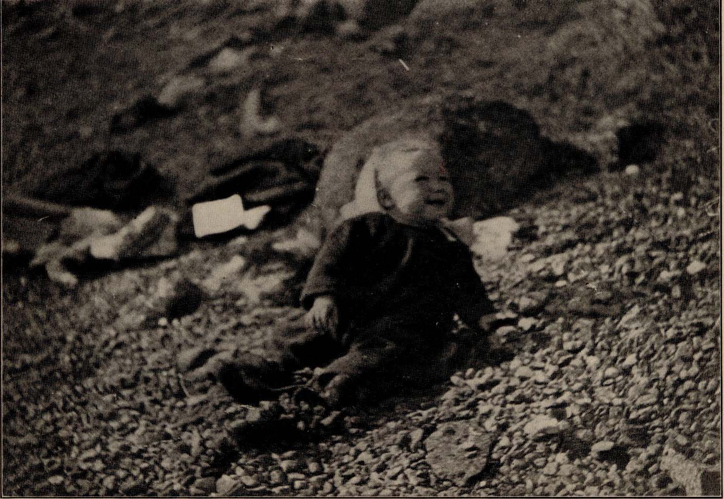 Baby sitting on hillside in a Gray Gown.