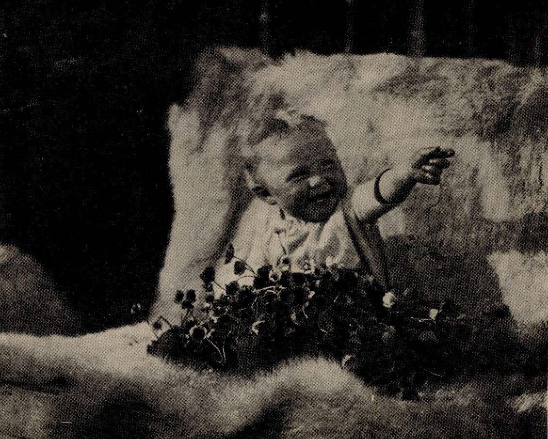 Baby holding out one of a pile of flowers.