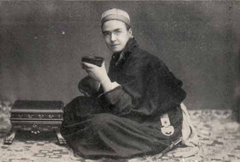man in glasses and robe seated cross-legged holding a bowl