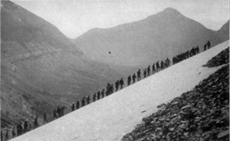 Line of hikers going up a steep incline with a huge mountain in the background. The hikers look tiny in comparison.