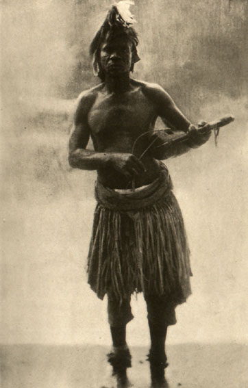 man in grass skirt holding musical instrument