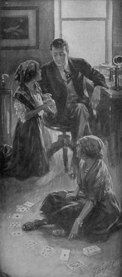 Two girls in gypsy clothing: one holds the hand of a young man seated in a chair, another deals cards on the floor