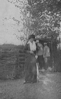 woman standing in front of earthen military barrier with two men facing away in background