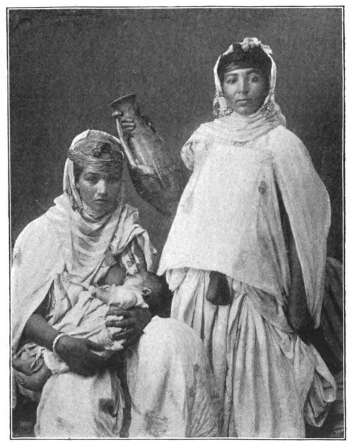 two women, one standing and one sitting with a baby