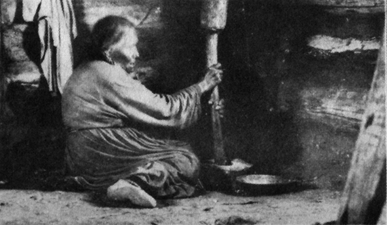 woman sitting on ground using mortar and pestle to grind corn