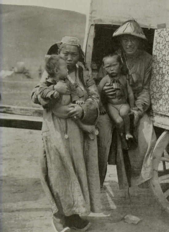 man and woman with two children, all seated and standing at the front of a cart
