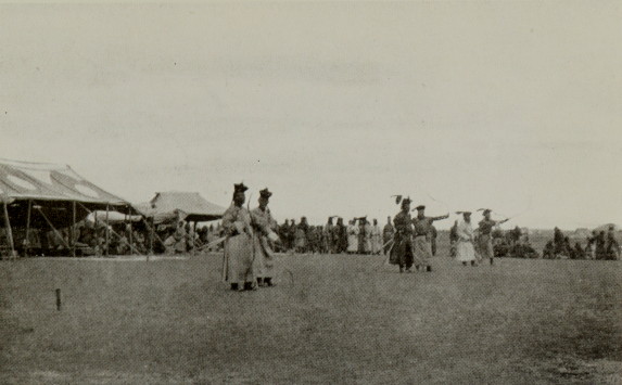 three pairs of archers standing in a field with many onlookers