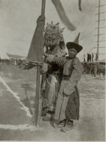 child and masked figure standing with large pole