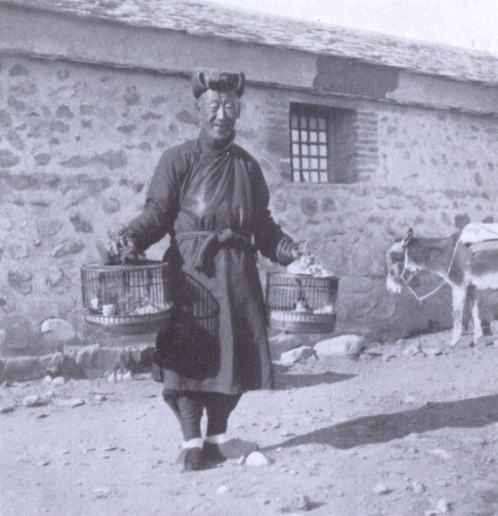 Chinese man carrying birdcages standing in front of a low stone building