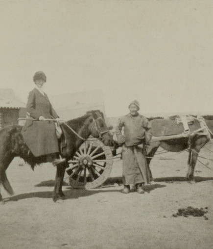 author sitting astride a horse, standing next to a Mongolian man and a horse-drawn cart