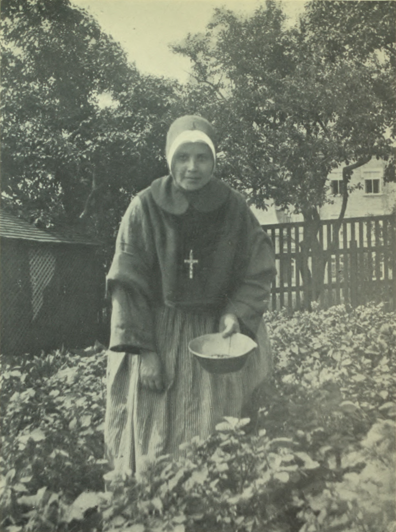 Nun in habit with a bowl, gathering something from the garden.