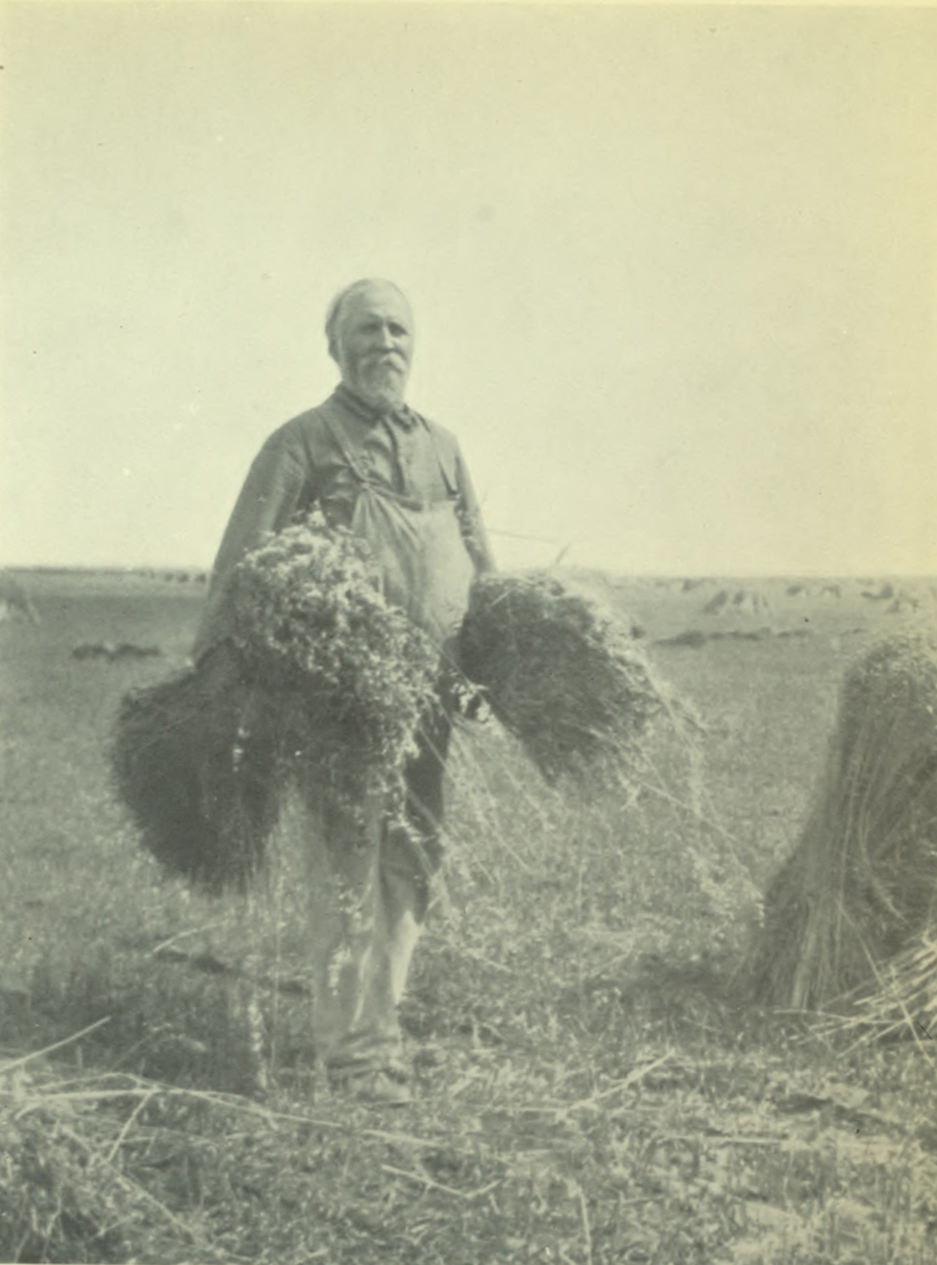 Man smiling, standing tall and proud, each hand filled with grain.