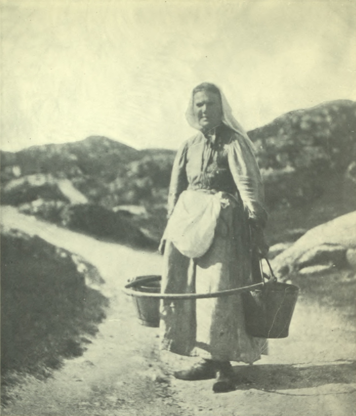 Woman in long dress with several baskets around her legs attached to a hoop.