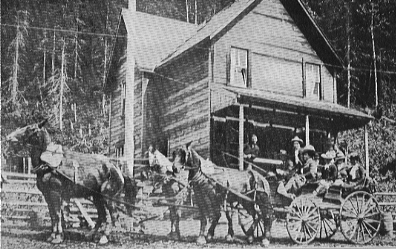 people in carriage drawn by four horses in front of wooden house