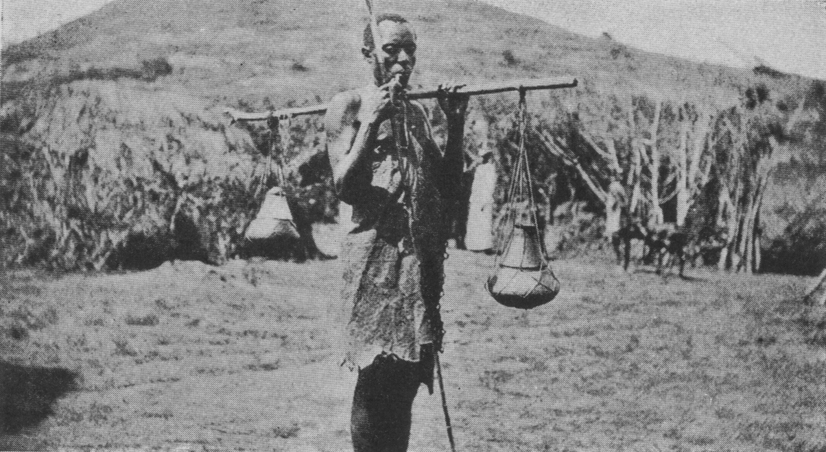 man with walking stick carrying two vessels on either end of a stick resting on his shoulder