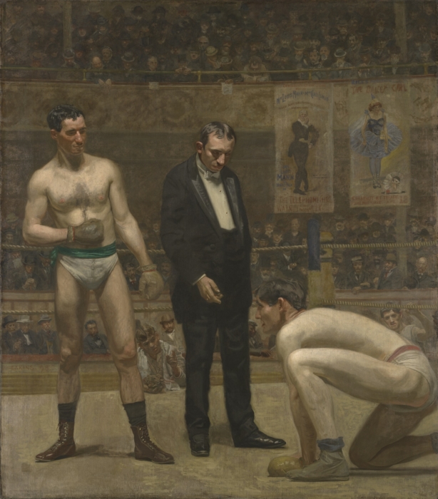man in suit standing between two wrestlers
