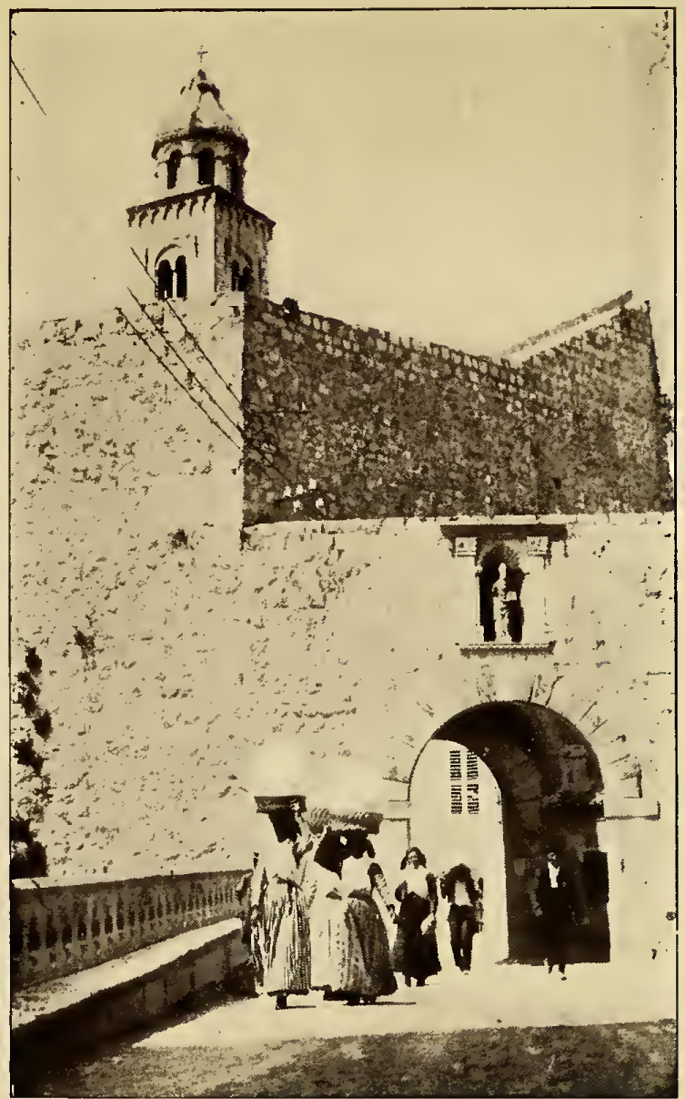 Small arched gateway in wall over street with foot traffic. Caption: Ragusa Porte Plocce and St. Biagio.