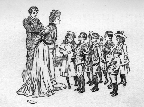 Children standing in a group facing the woman and a man with his arms crossed.