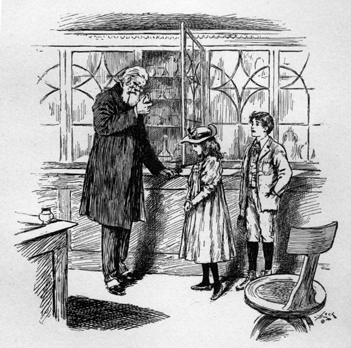 Two children standing beside a tall man with a beard who is leaning against a cabinet examining the object in his hand.