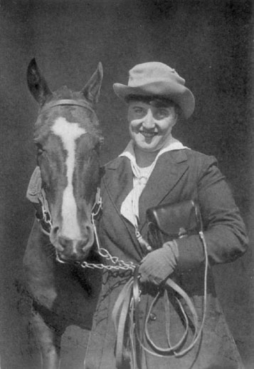 Photograph of a woman in a hat holding the bridle of a horse.