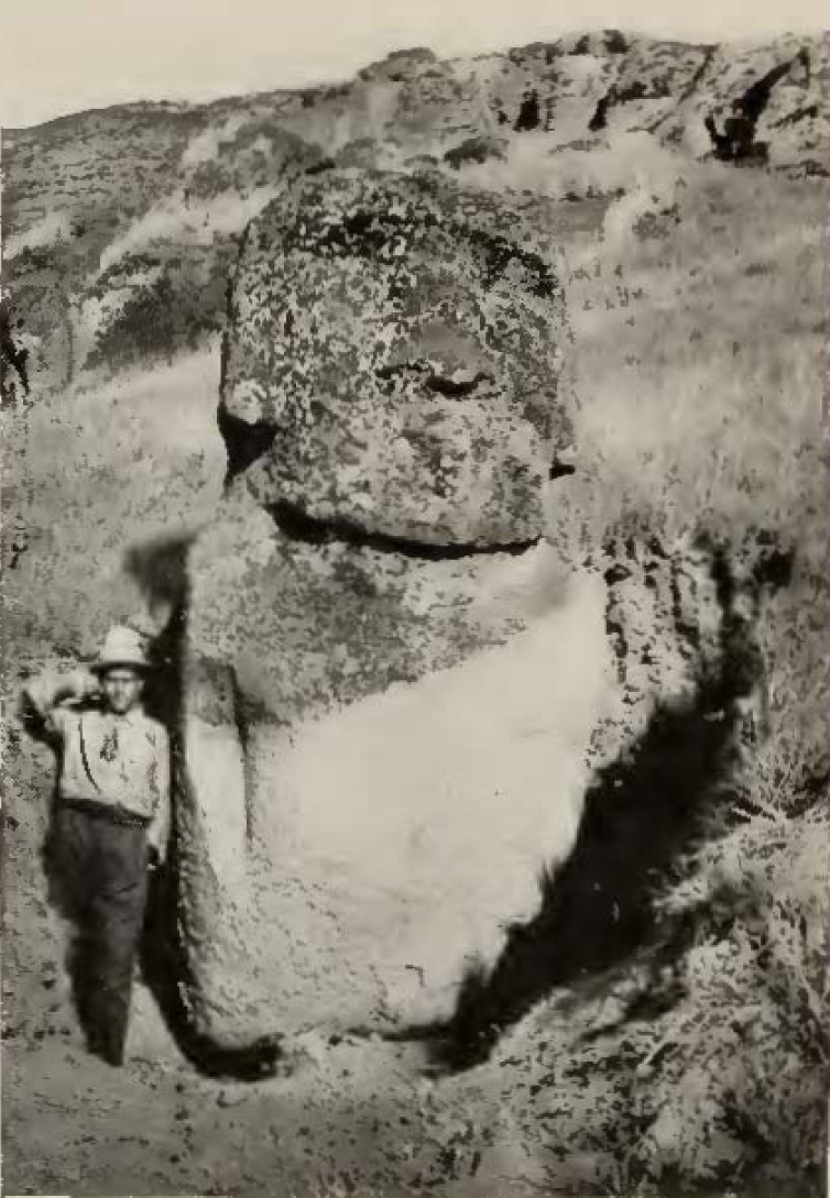 man standing next to stone statue partially dug out of the ground