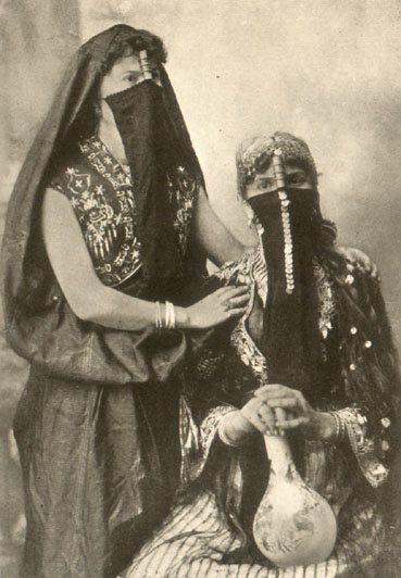 two women in embroidered or beaded garments with head and face scarves