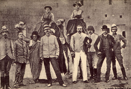Group photo of a row of men with two women on camels behind them.
