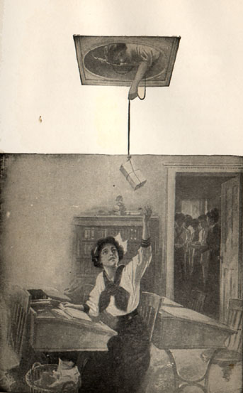 girl seated at a desk catches box being lowered from space in the ceiling