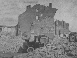car surrounded by rubble from bombed-out buildings; ruins of one such building visible in background
